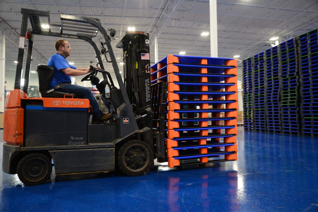 Person operating a forklift with stacked orange pallets in a warehouse.