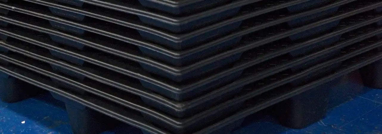 Stack of black plastic pallets on a blue surface