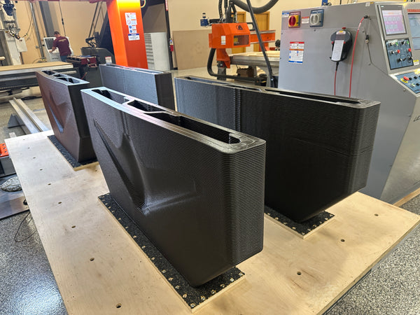 Industrial 3D printer printing large black parts in a warehouse setting.