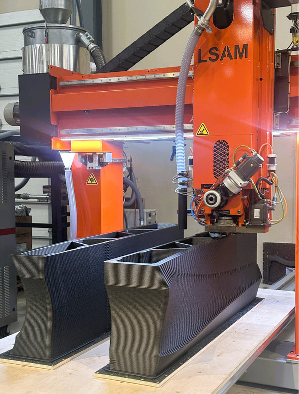 Industrial 3D printer printing large black parts in a warehouse setting.