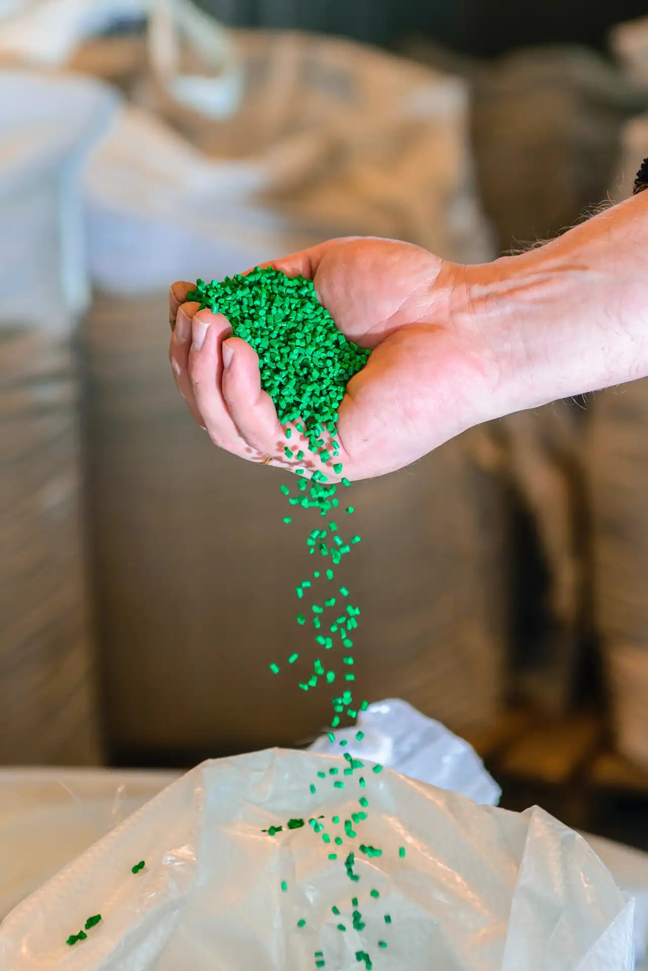Hand pouring green plastic pellets onto a white surface with a blurred background