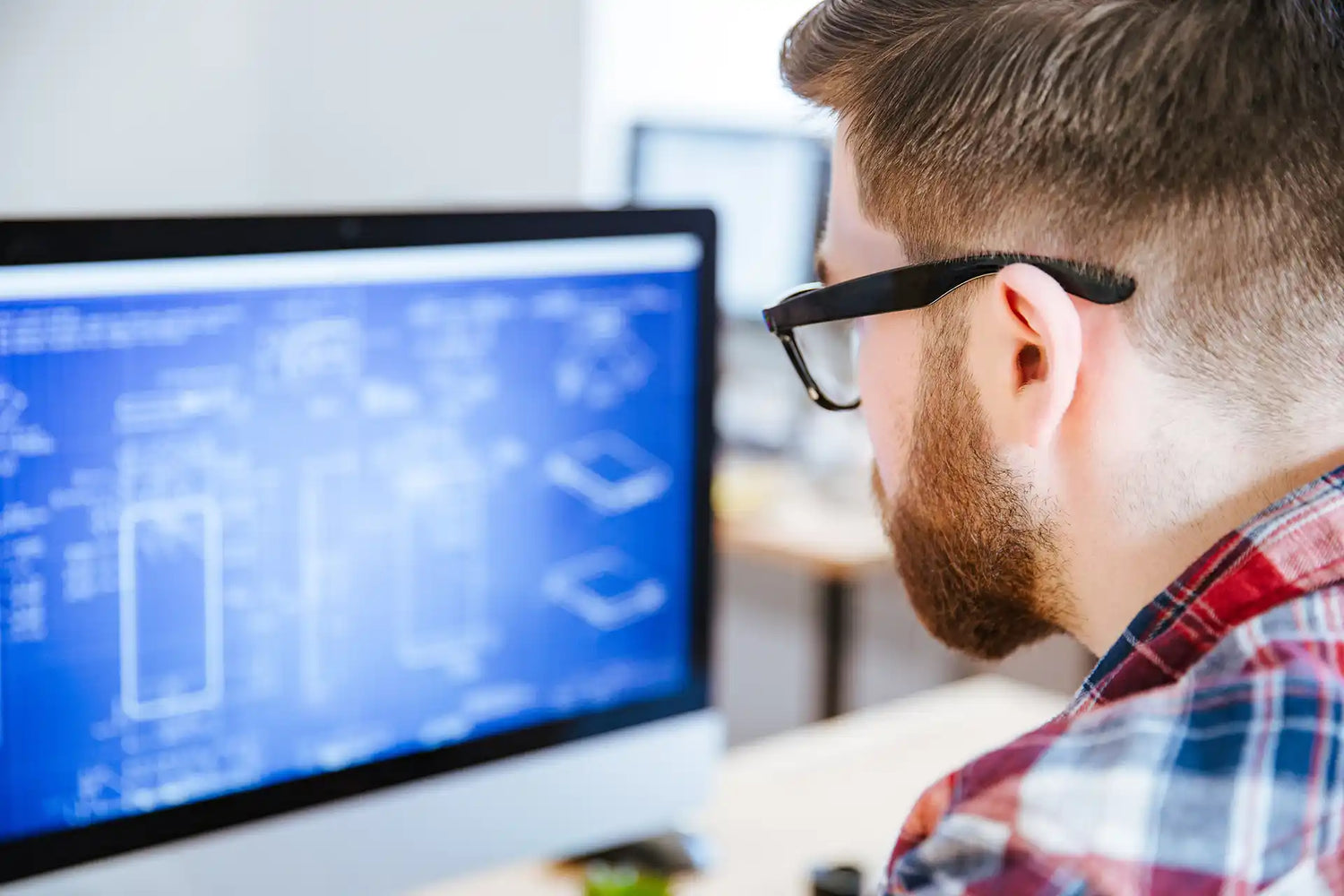 Person wearing glasses looking at a computer screen with blueprints on it