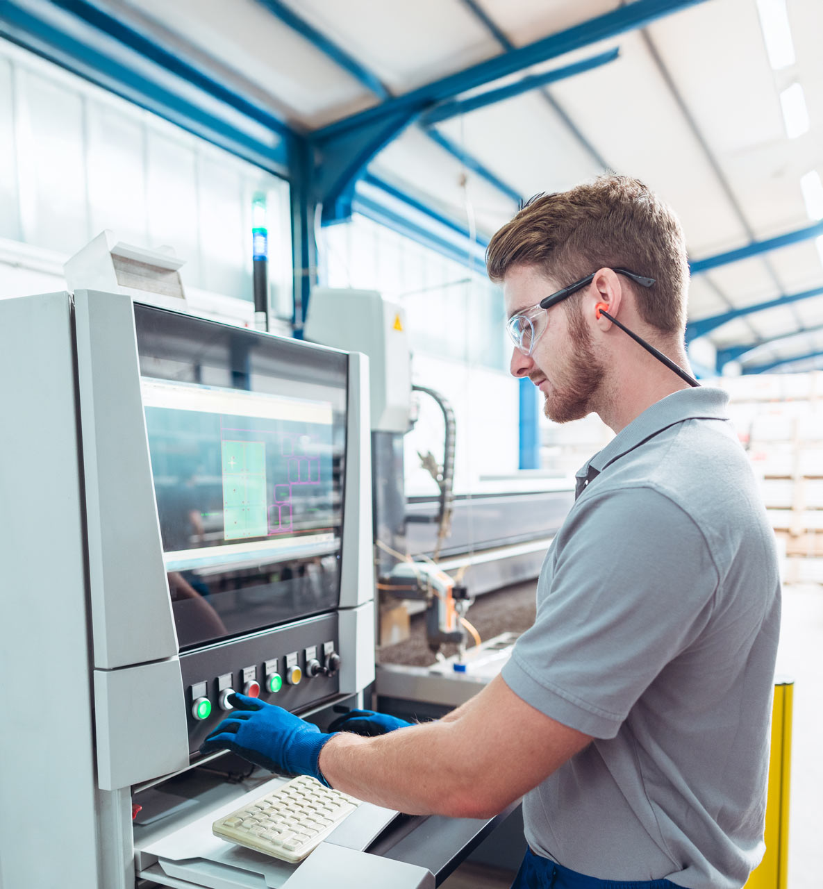 Man operating a machine with a computer interface in an industrial setting