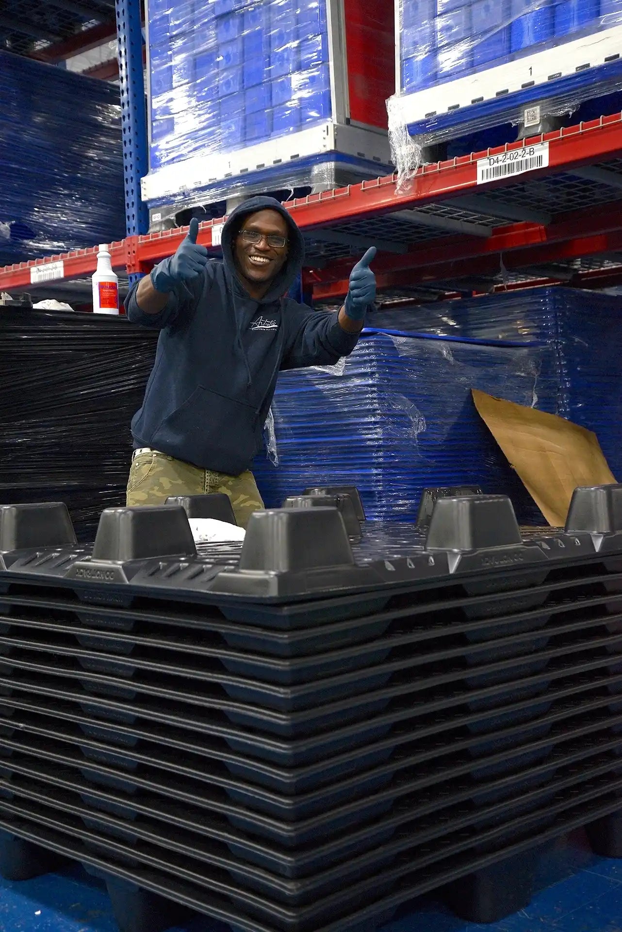 Person standing among stacked pallets and blue containers in a warehouse setting